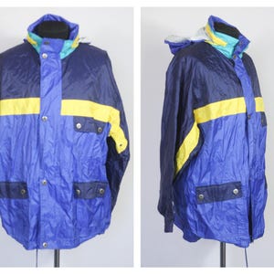 Könnte beinhalten: Eine blaue, gelbe und marineblaue Farbblockjacke mit Reißverschluss und Druckknopfverschluss. Die Jacke hat eine Kapuze und zwei Taschen.