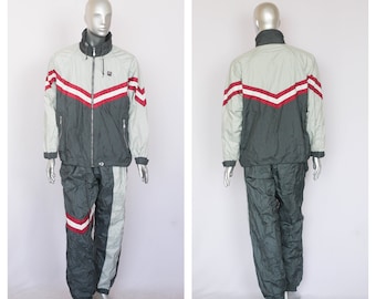 May include: A two-piece tracksuit in green and gray with red and white stripes. The jacket has a zipper closure and two pockets. The pants have an elastic waistband and two pockets.