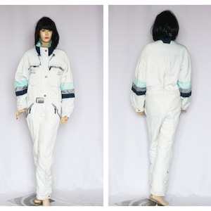 May include: White ski suit with blue and light blue stripes on the sleeves. The suit has a zipper closure and a belt.