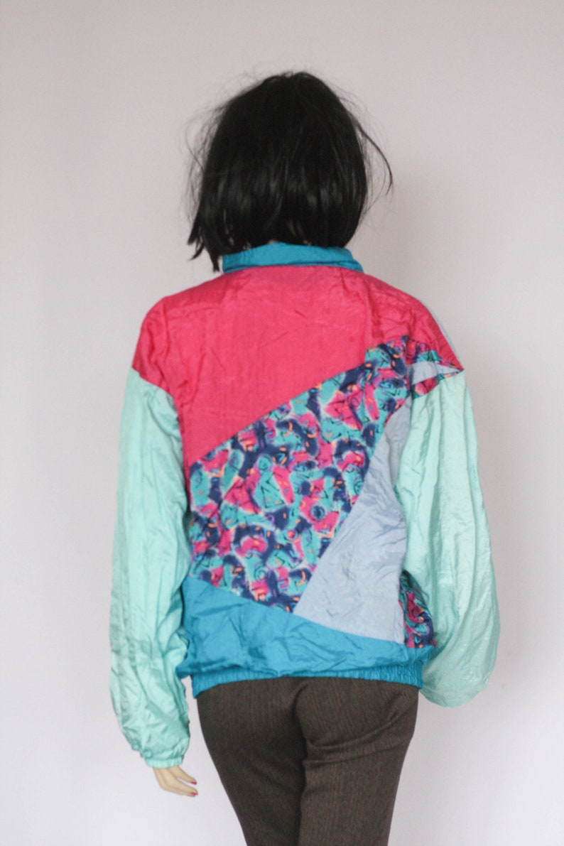 Puede incluir: Una chaqueta colorida, multicolor con un dise&ntilde;o geom&eacute;trico. La chaqueta est&aacute; hecha de una tela ligera de nylon y tiene una cremallera. La chaqueta est&aacute; en un esquema de colores turquesa, rosa, azul y blanco.
