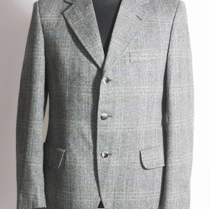 Pu&ograve; includere: Un blazer grigio con un motivo a quadri blu e bianco. Il blazer ha una chiusura a un solo bottone con tre bottoni.