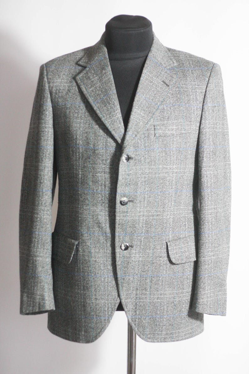 Pu&ograve; includere: Un blazer grigio con un motivo a quadri blu e bianco. Il blazer ha una chiusura a un solo bottone con tre bottoni.