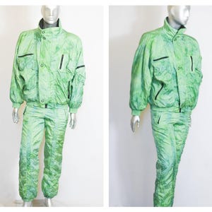 Puede incluir: Un traje de esquí verde con una chaqueta con cremallera y pantalones a juego. El traje tiene un patrón de tie-dye y está hecho de un material brillante e iridiscente.