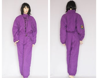 May include: A purple ski suit with a lace-up front and a patch on the sleeve.