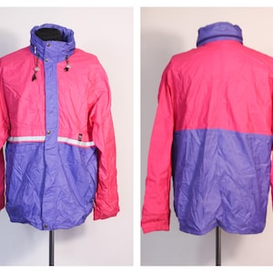 Peut inclure: Une veste imperméable rose et violette avec une fermeture éclair et une capuche. La veste a une bande réfléchissante sur la poitrine.