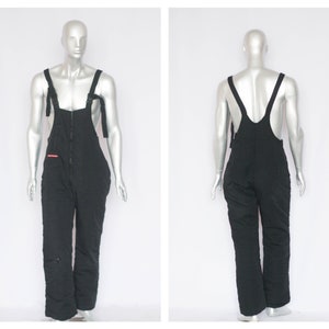 May include: Black quilted ski overalls with adjustable straps and a zipper closure.