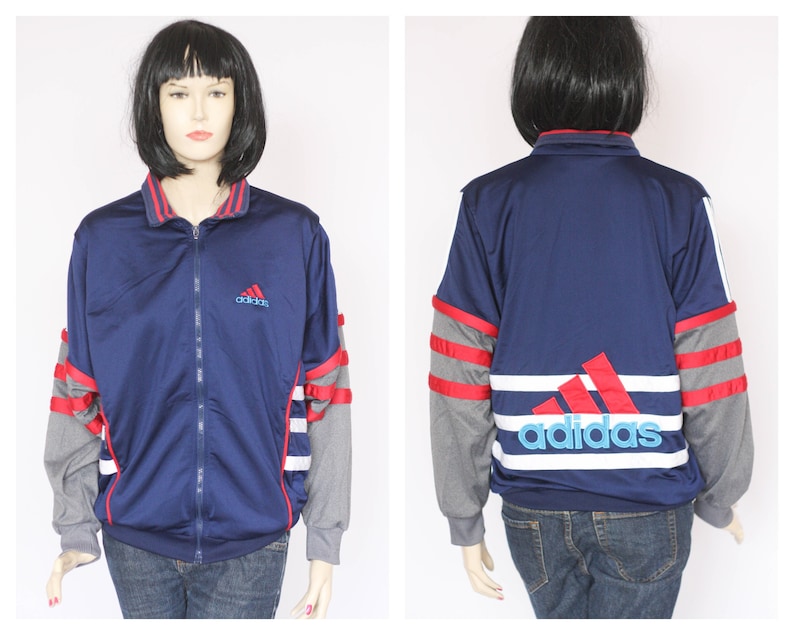 Peut inclure: Une veste zipp&eacute;e bleu marine avec des rayures rouges et blanches sur les manches et un grand logo Adidas blanc et bleu au dos. La veste a un petit logo Adidas brod&eacute; sur la poitrine gauche.
