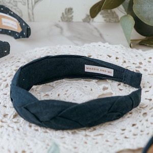 May include: A dark navy blue braided headband made of linen fabric. The headband has a label that says "MADDIE AND ME".