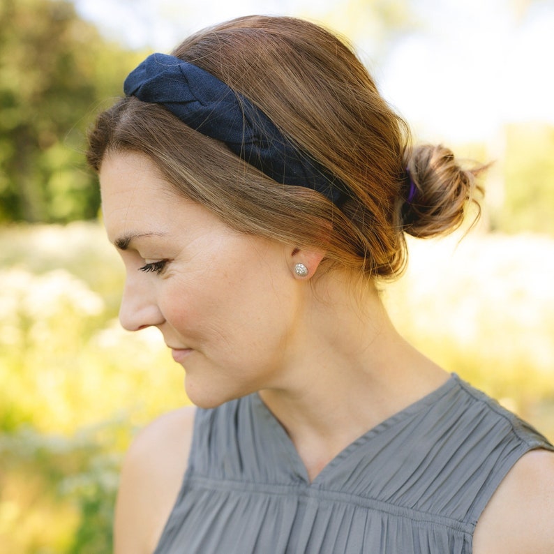 May include: A woman with brown hair wearing a dark blue headband and a gray sleeveless top. She is looking down and has a serious expression on her face.