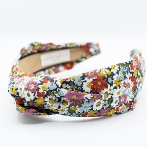 May include: A floral headband with a knotted design. The headband has a label that says "MADDIE AND ME".