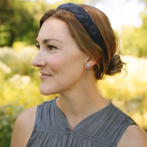 May include: A woman with brown hair wearing a dark blue braided headband and a gray sleeveless top. She is looking to the right and smiling.