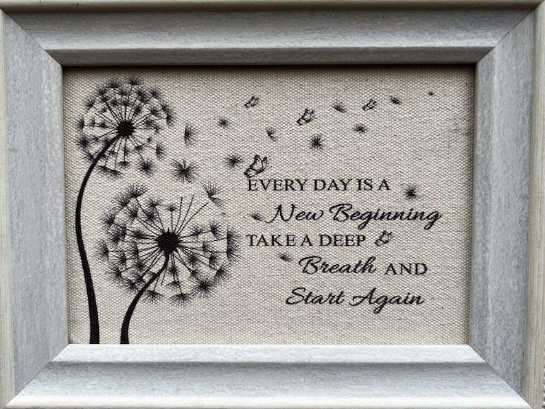 May include: Framed canvas print with a quote about new beginnings. The quote reads "Every day is a new beginning. Take a deep breath and start again." The print features two black dandelion silhouettes with seeds blowing in the wind.