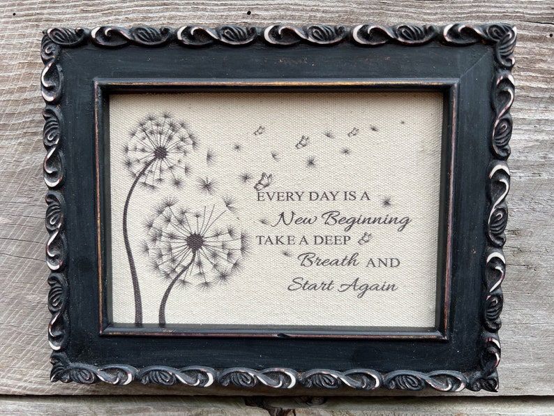 May include: A framed print with a burlap background featuring two dandelion illustrations and the text "Every day is a new beginning. Take a deep breath and start again."