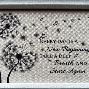 May include: A framed canvas print with a quote about new beginnings. The quote reads "Every day is a new beginning. Take a deep breath and start again." The print features two black dandelion silhouettes with seeds blowing in the wind.