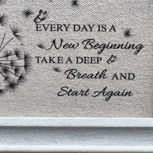 May include: A framed print with a black and white dandelion design and the text "Every day is a new beginning. Take a deep breath and start again."