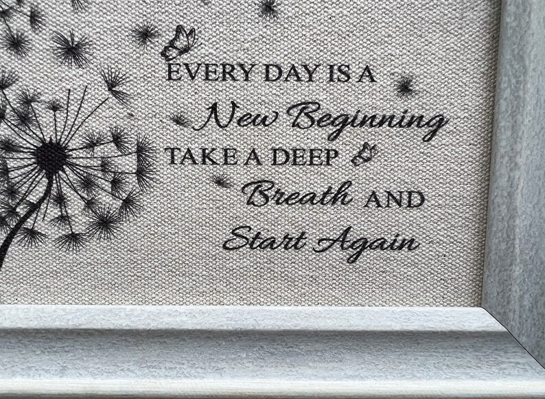 May include: A framed print with a black and white dandelion design and the text "Every day is a new beginning. Take a deep breath and start again."