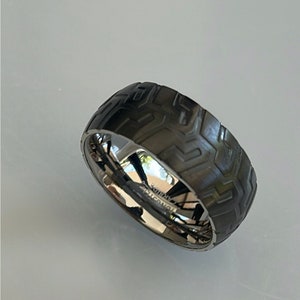 May include: A black and silver ring with a textured tire tread design. The ring is made of tungsten carbide.
