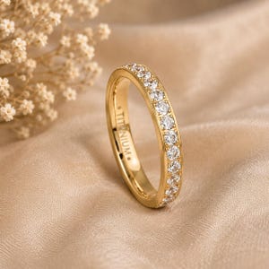 May include: A gold-toned titanium ring featuring a channel of small, clear, round-cut stones set along the outer band. The interior of the band is clearly engraved with the word TITANIUM in capital letters, visible on the inner surface.