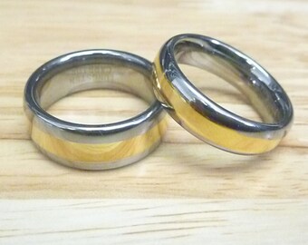 May include: Two matching wedding bands with a black and gold finish. The bands are made of tungsten carbide and have a gold inlay.