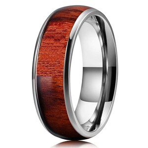 May include: A polished ring with a stainless steel band and a reddish-brown wood inlay. The wood grain is visible, adding texture to the ring's design. The ring has a smooth, reflective surface.