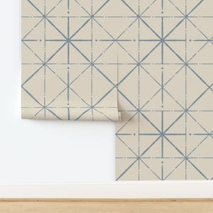 May include: A roll of wallpaper with a repeating geometric pattern. The design features light blue lines forming star-like shapes on a beige background. The wallpaper is partially unrolled, revealing the pattern.
