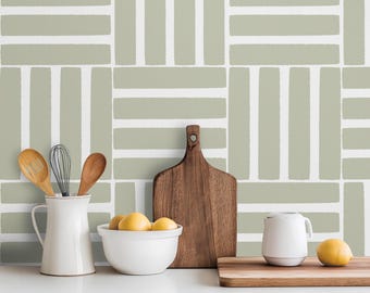 May include: A kitchen scene featuring a white countertop with a light green and white patterned wall. A wooden cutting board, a white pitcher with wooden spoons, a bowl of lemons, and a white mug are on the counter. A single lemon sits on a wooden board.