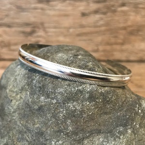 May include: A silver bangle bracelet with a beaded edge.