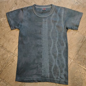 Può includere: Una maglietta blu tie-dye con un motivo a onde bianche sul lato destro.