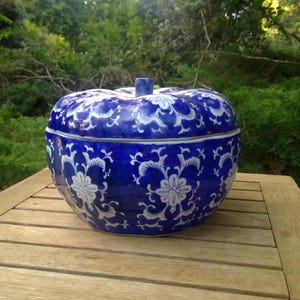 May include: A ceramic lidded jar shaped like a pumpkin, featuring a deep blue glaze with a white floral and scrolling vine pattern. The lid includes a small central stem handle, and the overall design is rounded with a segmented, ribbed surface.
