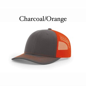 May include: A charcoal and orange trucker hat. The front of the hat is charcoal and the back is orange mesh.