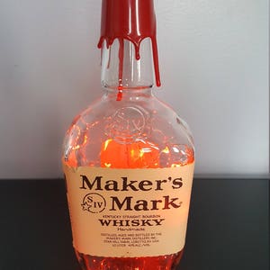 May include: A clear glass Maker's Mark bourbon bottle with a red wax seal. The bottle is filled with orange lights, and the label reads "Maker's Mark Kentucky Straight Bourbon Whisky". The bottle is handmade and contains 10 liters.