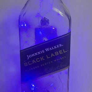 May include: A clear Johnnie Walker Black Label bottle with blue battery-operated lights inside. The bottle has a black label with white text and a black cap. The text "Johnnie Walker Black Label" is visible.
