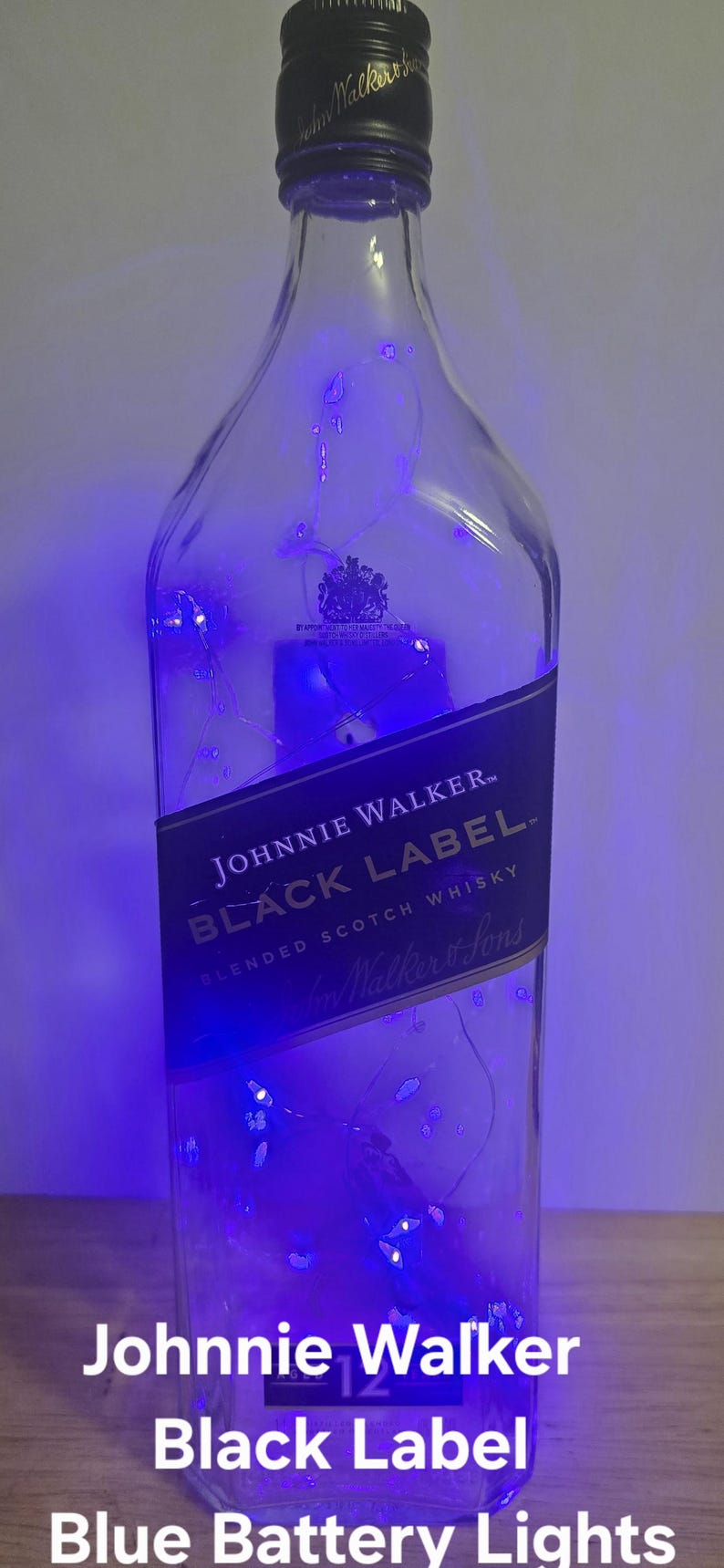 May include: A clear Johnnie Walker Black Label bottle with blue battery-operated lights inside. The bottle has a black label with white text and a black cap. The text "Johnnie Walker Black Label" is visible.