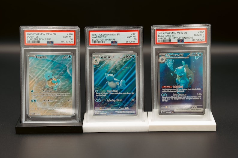 May include: Three Pokemon trading cards in protective cases. The cards are graded Gem Mint 10 and feature Squirtle, Wartortle, and Blastoise ex. The cards are from the 2023 Pokemon Mew En set.
