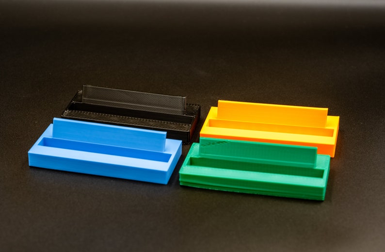 May include: Four plastic storage containers in different colors: black, blue, orange, and green. Each container has a rectangular shape with a raised lip on one side.