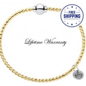 May include: A gold-toned twisted wire bracelet featuring a smooth silver-toned spherical bead at the top center and a small circular silver-toned charm with an engraved sun and wave design hanging from the bottom right side.