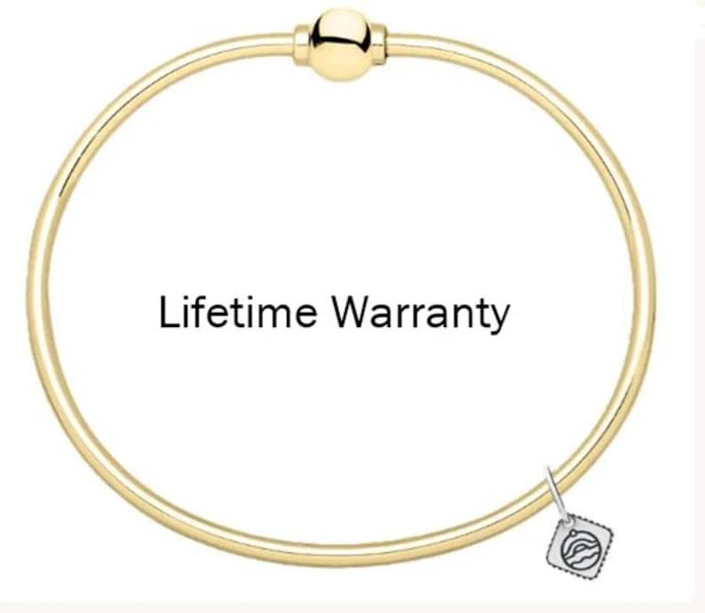 May include: A gold-toned circular bangle bracelet featuring a central spherical clasp and a small square charm with a wave-like graphic design. The text "Lifetime Warranty" is printed in the center of the circular bangle.