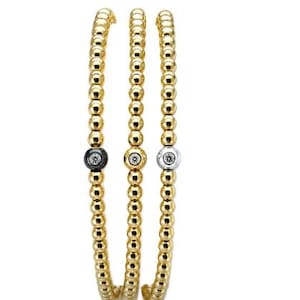 May include: Three gold beaded bracelets. One bracelet features a black bead with a white center, another has a gold bead with a white center, and the third has a silver bead with a white center. The bracelets are flexible and round.