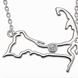 May include: A silver-toned necklace featuring a pendant shaped like the outline of Cape Cod. The pendant is crafted from polished metal and includes a single, small, round, clear faceted stone set into the center of the landmass shape.