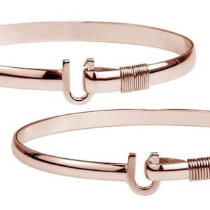 May include: Two rose gold bangles. Each bangle features a U-shaped clasp and a wrapped wire detail near the clasp. The bangles are smooth and shiny, reflecting light.