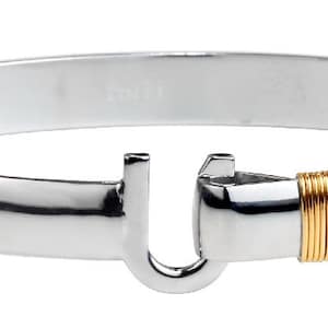 May include: A polished silver bangle bracelet with a hook clasp. The clasp and a section of the bracelet are accented with gold-colored wire. The bracelet has a smooth, rounded design.