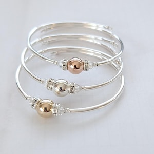 May include: Three silver bangle bracelets with a single bead accent. The beads are gold, silver, and rose gold.