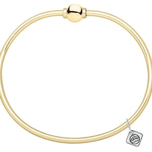 May include: A gold-toned circular bangle bracelet featuring a smooth, polished finish and a central spherical bead closure. A small, square-shaped silver-toned charm with a graphic line drawing of waves is attached to the side of the bangle band.