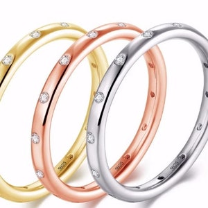 May include: Three delicate rings in gold, rose gold, and silver, each adorned with small, evenly spaced clear gemstones. The rings are stacked, showcasing their different metallic finishes and sparkling accents. The rings are marked with "S925".