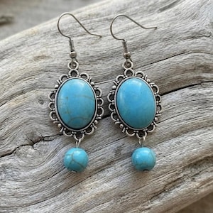 May include: A pair of dangle earrings featuring oval-shaped turquoise-colored stones with dark veining, set in ornate silver-toned metal frames. Each earring includes a smaller round turquoise-colored bead suspended below the main oval setting.