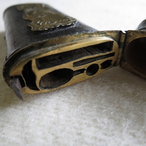Op de afbeelding: Een vintage, leren, messingkleurige, scharnierende doos met een compartiment voor het bewaren van kleine voorwerpen. De doos is open en onthult een compartiment met een klein, decoratief metalen ontwerp.