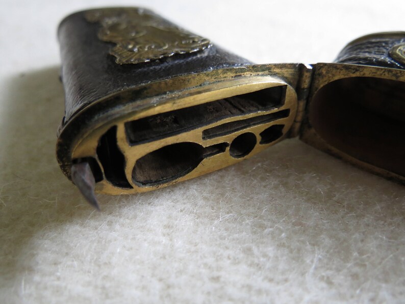 Op de afbeelding: Een vintage, leren, messingkleurige, scharnierende doos met een compartiment voor het bewaren van kleine voorwerpen. De doos is open en onthult een compartiment met een klein, decoratief metalen ontwerp.