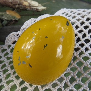 Pu&ograve; includere: Un oggetto giallo a forma di uovo con una superficie lucida leggermente usurata. L'oggetto presenta alcune piccole macchie grigio scuro.