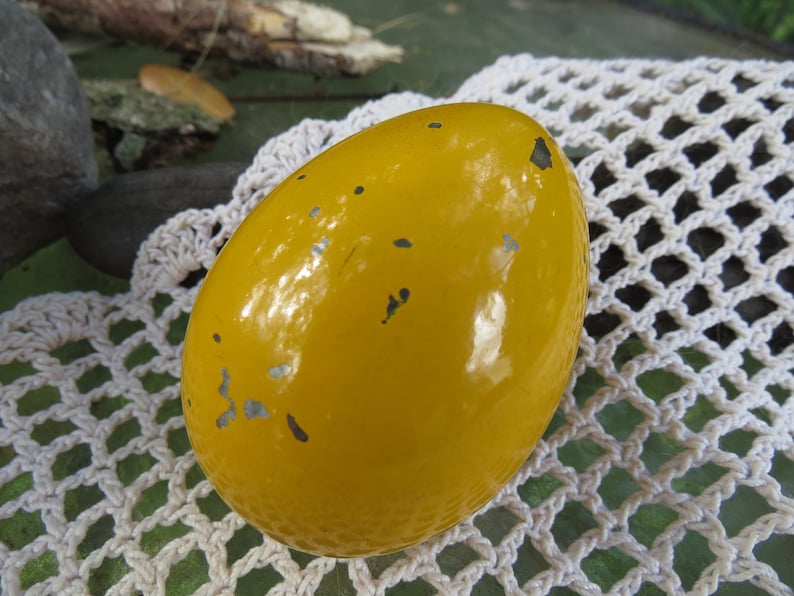 Pu&ograve; includere: Un oggetto giallo a forma di uovo con una superficie lucida leggermente usurata. L'oggetto presenta alcune piccole macchie grigio scuro.