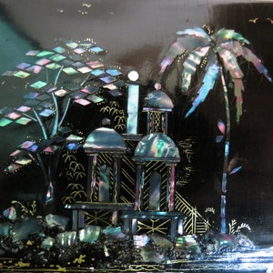 Pu&ograve; includere: Una scatola laccata nera con una scena di un pagoda e palme intarsiate con madreperla iridescente. La scena &egrave; delineata con vernice dorata.